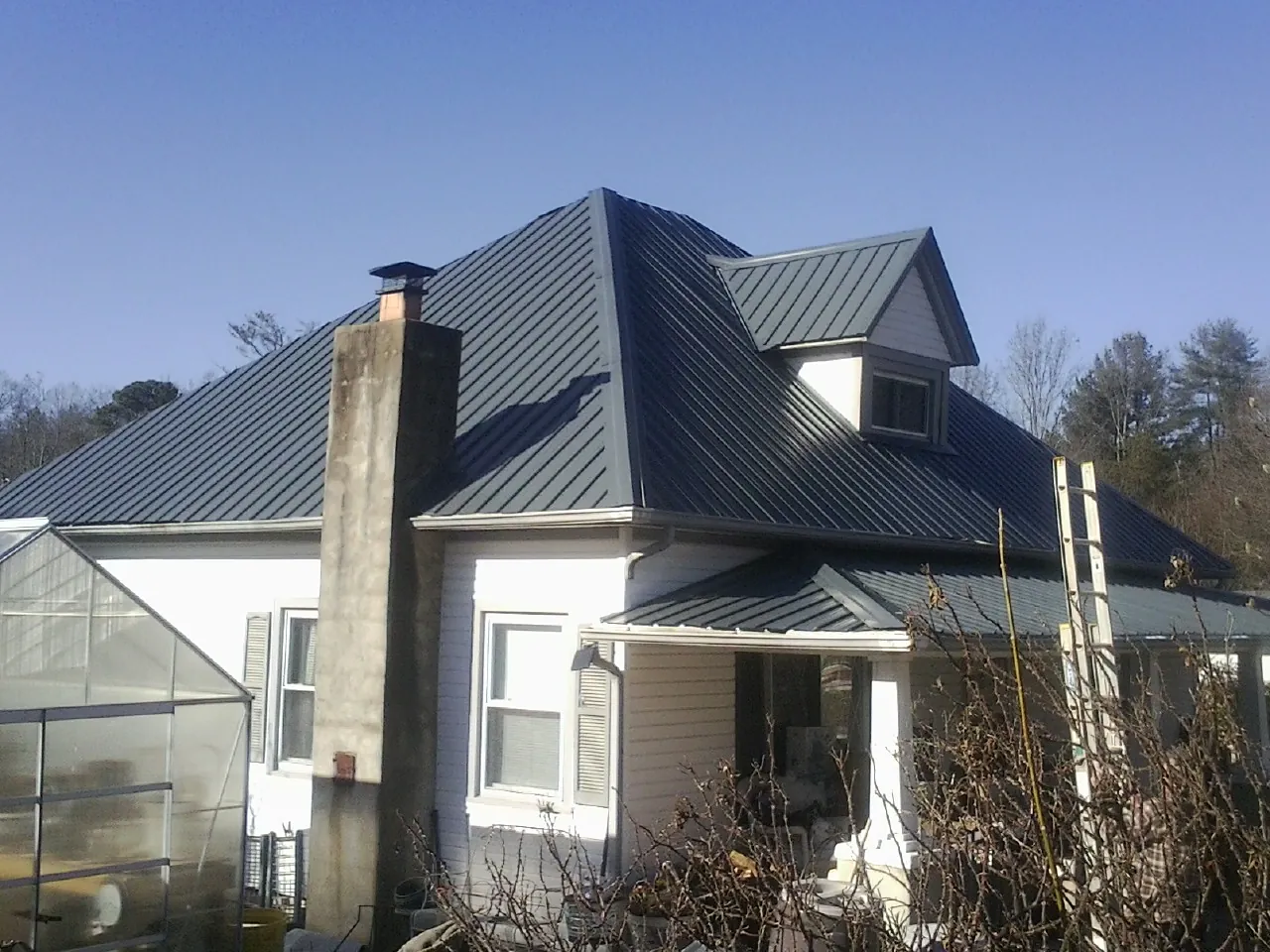 Dark blue standing seam metal roof on a white farmhouse with dormer — Slate & Tile Roof Repair by Roofing Brothers in Hamer