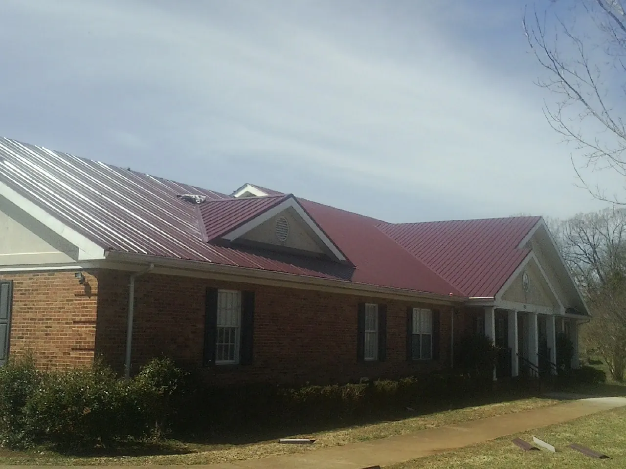 Red metal roof with gabled entries on a long brick building, from a Hail Damage Roof Repair job in Hamer