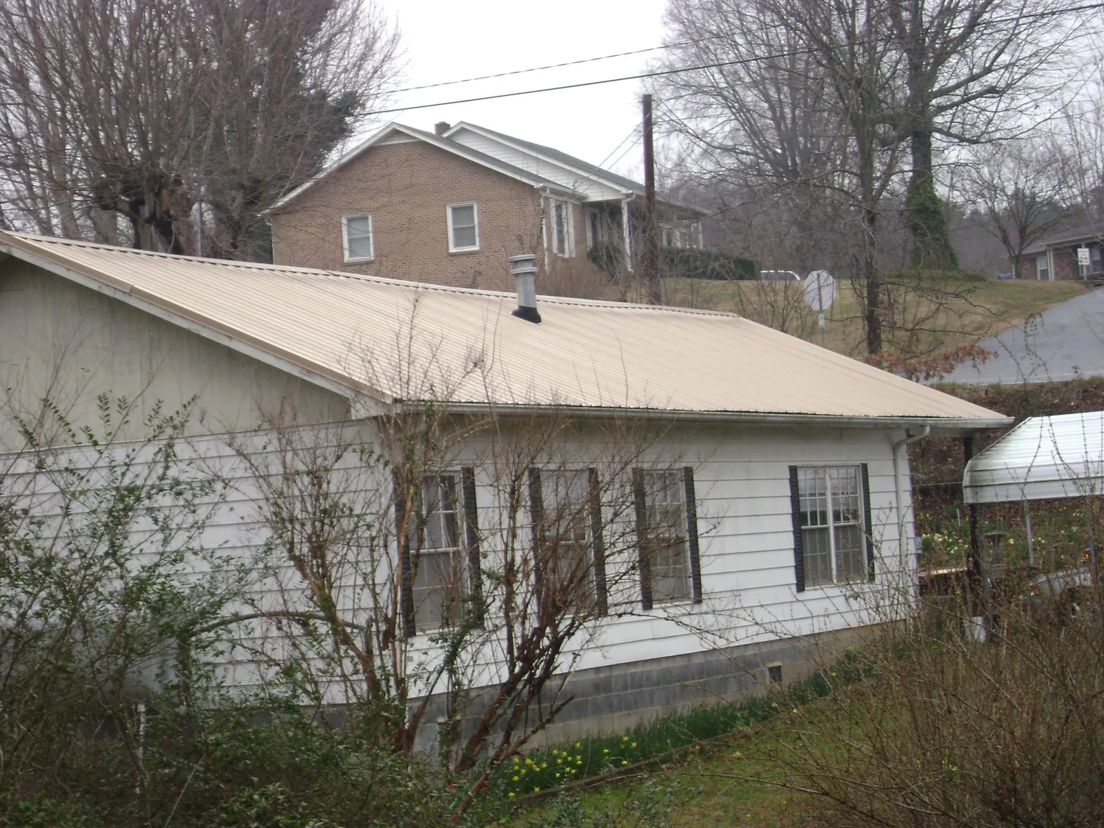 Tan metal roof on a white sided house set into a hillside — Commercial Roofing by Roofing Brothers in Hamer