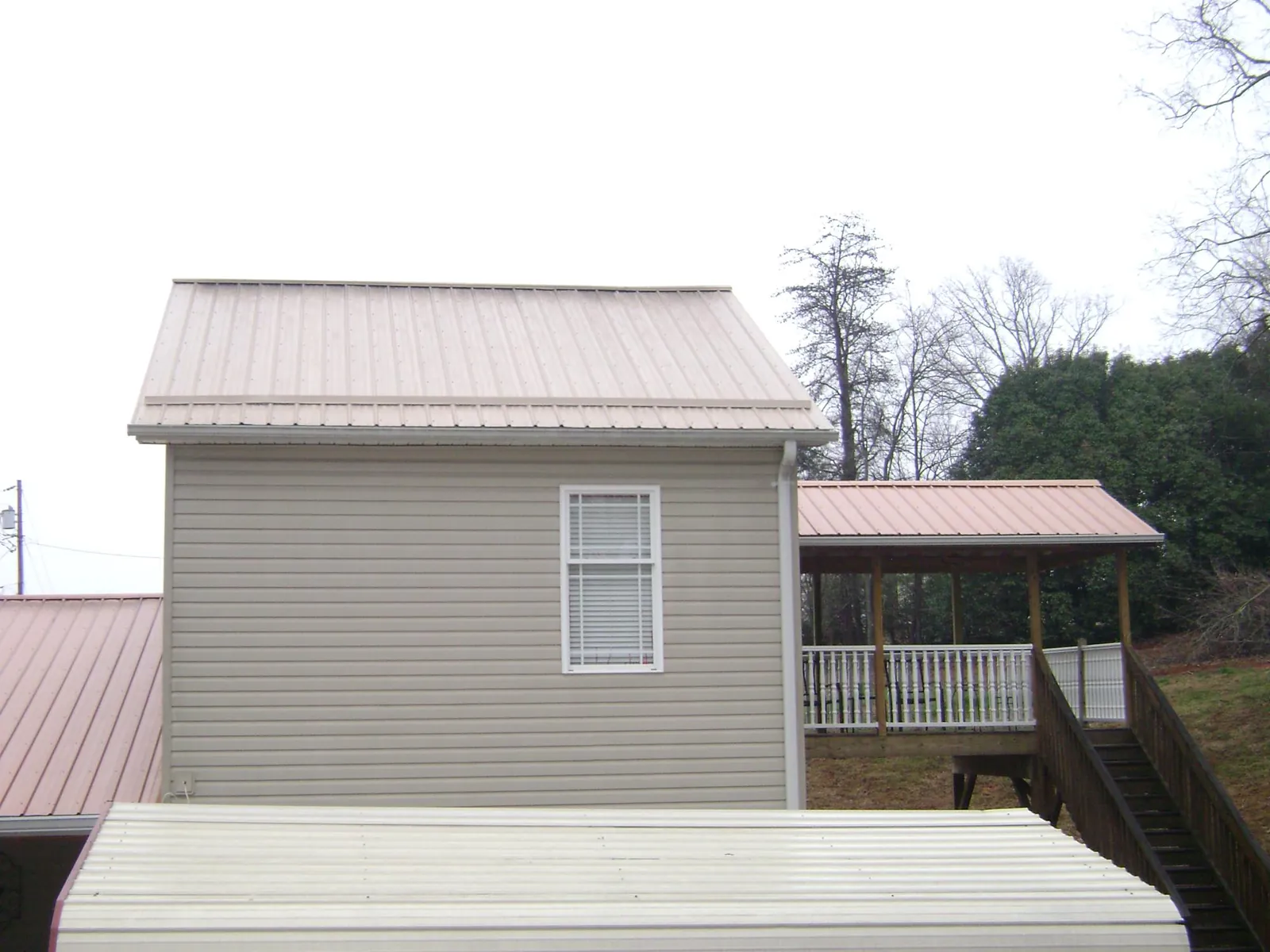 Tan metal roofs on a two story addition and attached porch, from a Roof Replacement job in Hamer